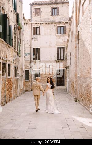 Mariage en Italie à Venise. La mariée et le marié marchent le long des rues désertes de la ville. Les jeunes mariés marchent dans un cul-de-sac Banque D'Images