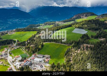 Vue aérienne de la ferme de piles solaires sur les pentes vertes des montagnes de l'Italie, Trentin, nuages énormes sur une vallée, toits de Banque D'Images