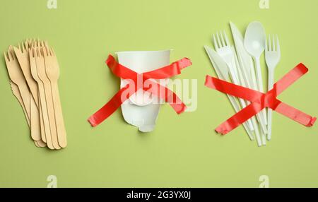 Fourchettes et cuillères en plastique collées avec du ruban rouge sur un fond vert, évitant le plastique Banque D'Images