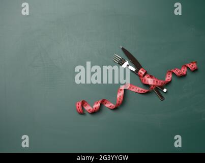 Fourche et couteau enveloppés de ruban de mesure vert sur fond vert Banque D'Images