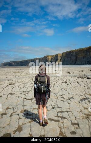 Femme marchant le long d'un rivage rocheux à Nash point, pays de Galles. Banque D'Images