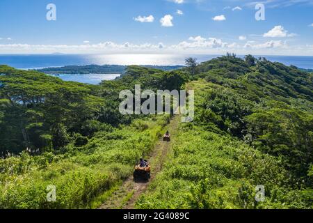 Vue aérienne de véhicules tout-terrain quad sur route de terre à travers la végétation luxuriante de montagne, Bora Bora, îles Leeward, Polynésie française, Pacifique Sud Banque D'Images