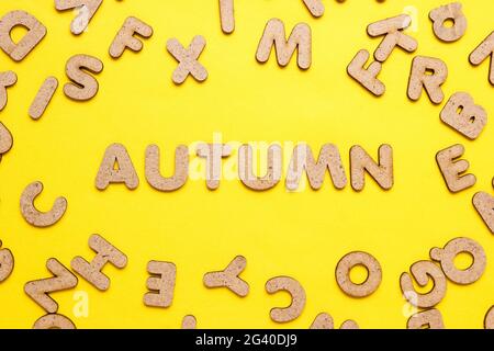 Le mot automne parmi des lettres en bois sur fond jaune. Vue de dessus Banque D'Images