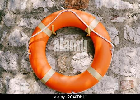 Bouée de sauvetage orange sur un mur en pierre grise. Banque D'Images