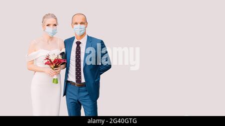 Mariée et marié dans des masques médicaux sur un fond isolé. Mariage pour deux durant l'isolement, pandémie Covid-19. Bannière avec cop Banque D'Images