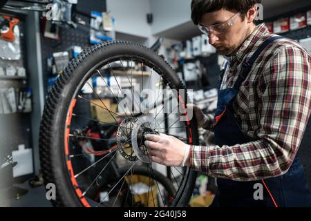 Homme mécanicien travaillant dans un atelier de réparation de vélos, mécanicien réparant le vélo à l'aide d'un outil spécial, portant des gants de protection. Jeune attra Banque D'Images