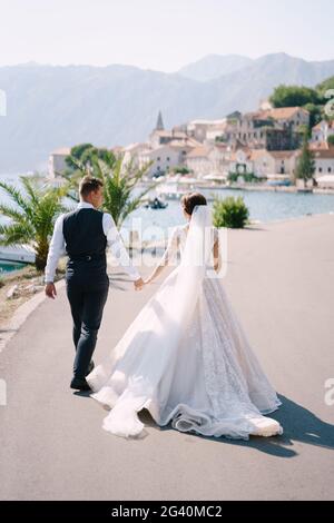 Photo de mariage des beaux-arts au Monténégro, Perast. Un couple de mariage marche le long de la promenade près de la mer, au milieu des palmiers, montagne Banque D'Images