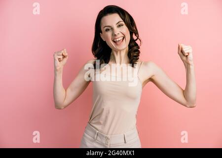 Belle dame attrayante avec des poings élevés, se réjouit sincèrement de sa victoire. Fille isolée sur fond rose avec espace de copie pour le texte. Banque D'Images