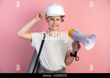 Jeune ingénieur est une fille sur fond de mur rose, elle porte un casque, des lunettes et un haut-parleur dans ses mains. Concept de construction. Banque D'Images