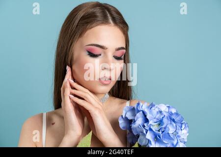 Douce, belle fille avec des fleurs sur fond bleu. Jolie fille touche son visage, pose magnifiquement, douce, belle fille avec des fleurs sur un bleu Banque D'Images