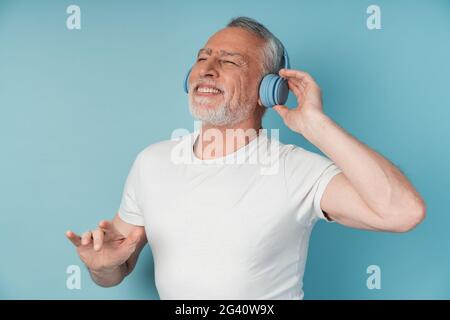 Un homme élégant et mature dans un casque aime la musique. Homme dansant isolé sur fond bleu., attrayant, homme mature dans le casque aime la musique. Homme da Banque D'Images