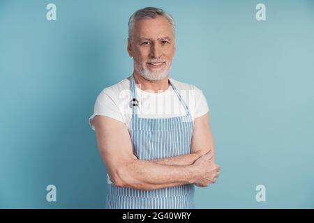 Beau, homme âgé dans un tablier bleu posant sur un fond bleu. Beau homme isolé sur fond de mur vierge Banque D'Images