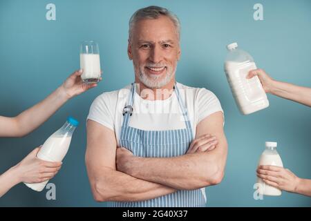 Beau homme souriant est debout sur un fond bleu, avec les mains des gens tenant le lait autour de lui, comme si lui était offert. Homme aux bras croisés. Banque D'Images