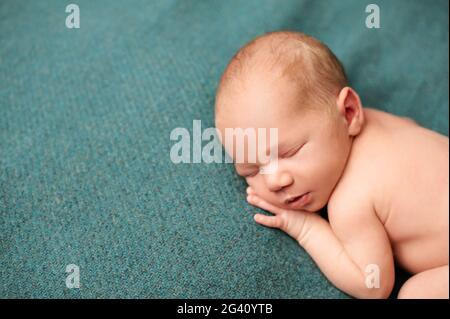 Portrait d'un nouveau-né dormant avec ses mains sous ses joues sur un fond turquoise. Banque D'Images