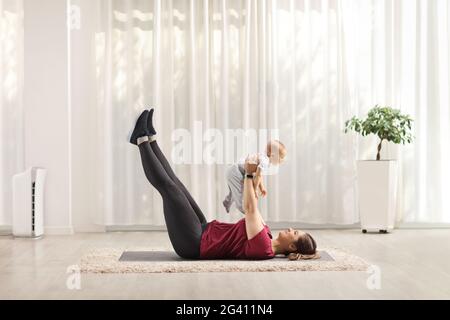 Jeune mère exerçant l'abs et tenant un bébé sur le sol à la maison Banque D'Images
