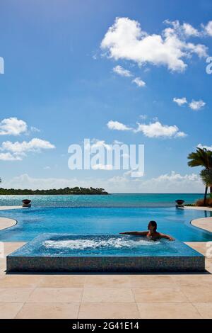 Une femme silhouetée a tiré dans un jacuzzi situé sur le côté d'une piscine à débordement. Tourné à Antigua, Antilles Banque D'Images