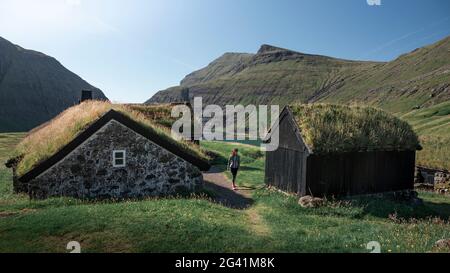 Femme dans des huttes avec des toits d'herbe dans le village de Saksun sur l'île de Streymoy, îles Féroé Banque D'Images