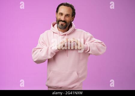 La famille dans le coeur. Portrait beau beau beau romantique barbu homme en rose hoodie passionatly regarder l'appareil photo montrer l'amour geste smili Banque D'Images