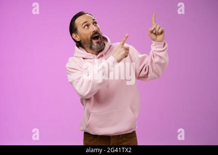 Enthousiaste charismatique grand-père sous tension barbu cheveux gris dans hipster moderne sweat à capuche pointant à l'air impressionné fasciné Banque D'Images