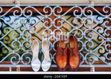 Nouvelles chaussures brunes pour hommes avec sandales blanches pour femmes sur la fenêtre à l'extérieur de la grille métallique. Banque D'Images