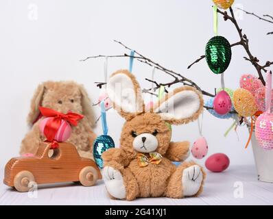 Un lapin en peluche sur fond blanc et des œufs de pâques décoratifs et colorés sont accrochés à une branche Banque D'Images