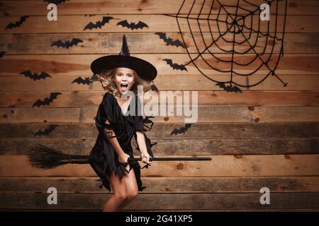Sorcière Halloween concept - petite sorcière caucasien enfant volant sur un balai magique et bat sur spider web l'arrière-plan. Banque D'Images