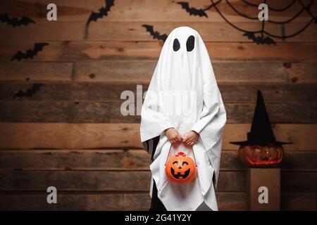 Halloween concept - petit fantôme blanc avec halloween potiron pot de bonbons faire le tour ou traiter avec des citrouilles incurvées sur les chauves-souris et Banque D'Images