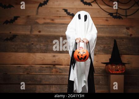 Halloween concept - petit fantôme blanc avec halloween potiron pot de bonbons faire le tour ou traiter avec des citrouilles incurvées sur les chauves-souris et Banque D'Images