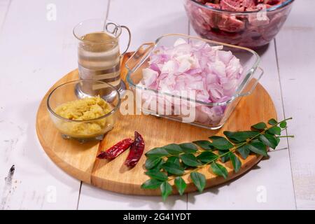 Ingrédients - oignon haché, pâte d'ail au gingembre, feuilles de curry, huile de cuisson et piment sec disposés sur une base en bois avec fond texturé. Banque D'Images