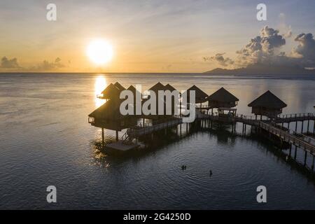 Vue aérienne des bungalows sur l'eau à Tahiti IA ora Beach Resort (géré par Sofitel) au coucher du soleil avec Moorea Island au loin, près de Papeete, Tahi Banque D'Images