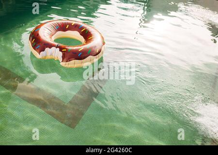 Un cercle de natation sous forme de donut mordu flotte dans l'eau de la piscine. Banque D'Images