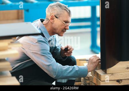 Un travailleur âgé restaure soigneusement les meubles dans un atelier de menuisier pendant la journée. Banque D'Images