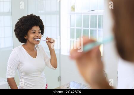 Femme afro-américaine debout dans la salle de bains se brossant les dents Banque D'Images