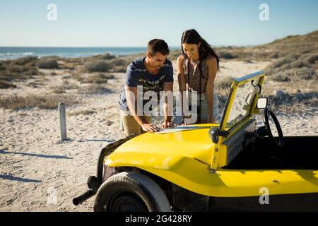 Couple caucasien heureux lisant la feuille de route sur la plage buggy à côté de mer Banque D'Images