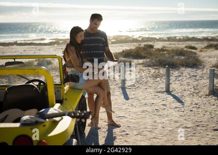 Heureux couple caucasien assis sur la plage buggy au bord de la mer lecture de la feuille de route Banque D'Images