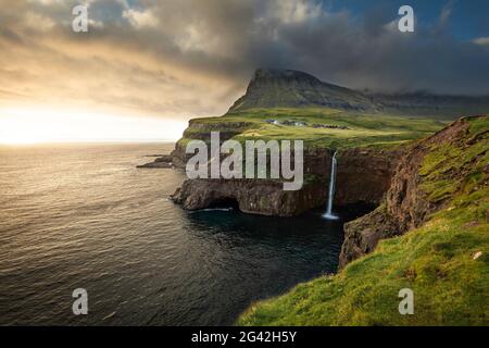 Coucher de soleil à la cascade de Múlafossur avec le village de Gásadalur sur l'île de Vagar, îles Féroé Banque D'Images