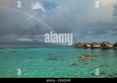 Les gens pagayent dans le lagon de Moorea avec vue sur l'arc-en-ciel et les bungalows sur l'eau du Sofitel IA ora Beach Resort, Moorea, Windward Isla Banque D'Images