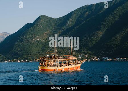 Bateau de plaisance rouge avec terrasse d'observation et passagers à bord, sur fond de montagnes verdoyantes de la baie de Ko Banque D'Images