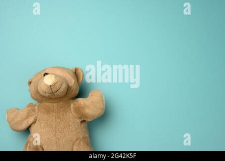 Le vieux ours en peluche avec un bracelet sur l'œil repose sur un fond bleu Banque D'Images