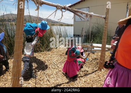 Enfants à l'école jouant sur une île flottante lac Titicaca Pérou jouer enfant fille garçon filles roseaux filles balançoires balançoire chapeau vêtements de couleur Banque D'Images