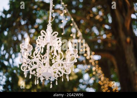 Lustre en cristal de six lumières et guirlande accrochée à l'arbre. Décoration d'un dîner de mariage à l'extérieur. Banque D'Images