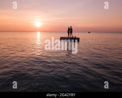 Vue aérienne silhouette de jeune couple debout sur une plate-forme de baignade au coucher du soleil sur la plage d'Ong Lang, Ong Lang, Phu Quoc Island, Kien Giang, Vietnam, ASI Banque D'Images