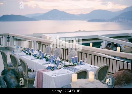 Réception de table de dîner de mariage avec beaucoup de bougies bleues épaisses contre le ciel de coucher de soleil sur les montagnes et la mer à Budva, Monténégro. Banque D'Images