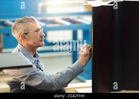 Un travailleur âgé restaure soigneusement les meubles dans un atelier de menuisier pendant la journée. Banque D'Images