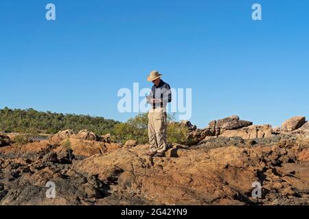 Cape Gloucester, Queensland, Australie - juin 2021 : retraité mâle debout sur des rochers tenant les commandes d'un drone alors qu'il le vole au-dessus du paysage Banque D'Images