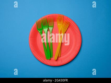 Fourchettes en plastique vert et orange et plaques jetables en papier rouge vides sur fond bleu Banque D'Images