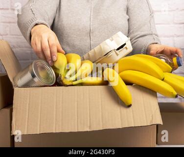 La femme recueille de la nourriture, des fruits et des choses dans une boîte en carton pour aider les personnes dans le besoin, aider et le concept de bénévolat Banque D'Images