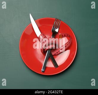 Plaque ronde rouge, fourchette et couteau enveloppés de ruban de mesure vert sur fond vert Banque D'Images