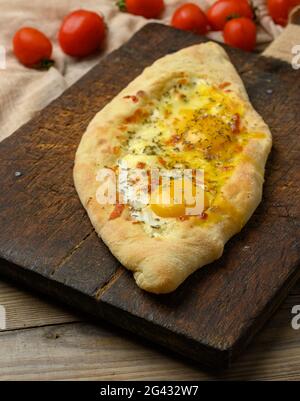 Khachapuri adjarien cuit au four avec du jaune d'œuf entier sur une planche en bois Banque D'Images