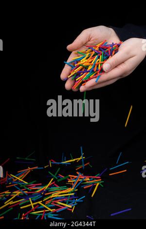 Main laissant des bâtons en bois de couleur tomber sur noir Banque D'Images